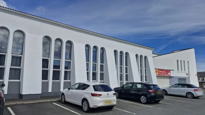 Long white hall with tall arched windows and grey bands at the base, cars parked in front