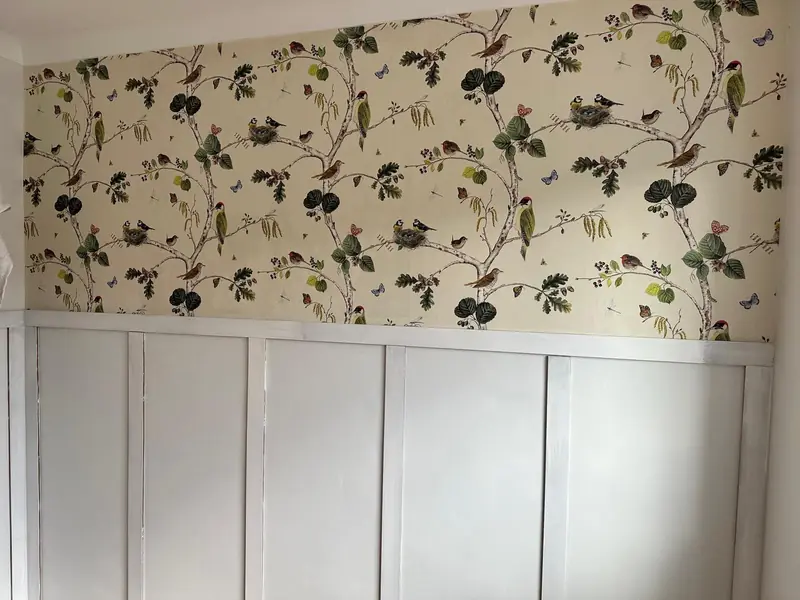 Bird and branch patterned wallpaper hung above freshly painted grey wall panelling