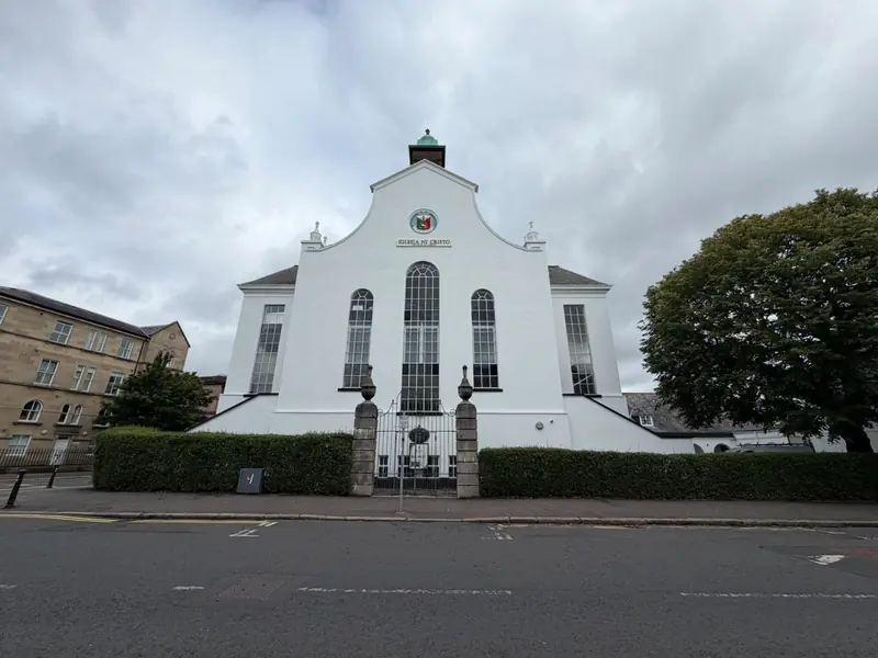 White-painted church front with a curved gable, tall arched windows and a small green cupola