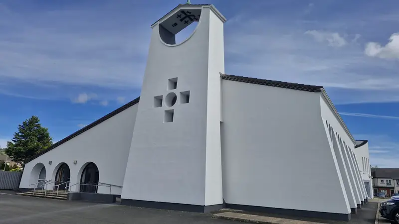 Modern church with a tall white tower and a cross of square windows, freshly painted under a blue sky