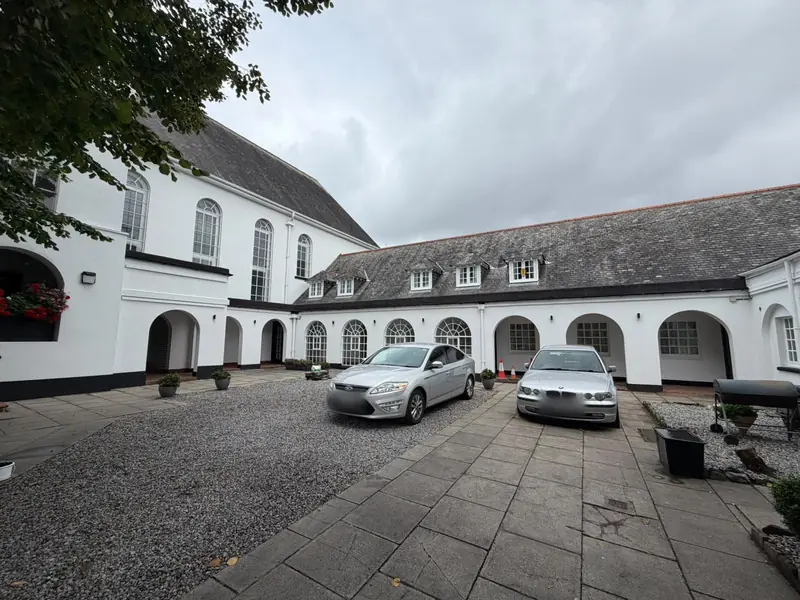 White-painted courtyard buildings with arched doorways, black plinths and a slate roof