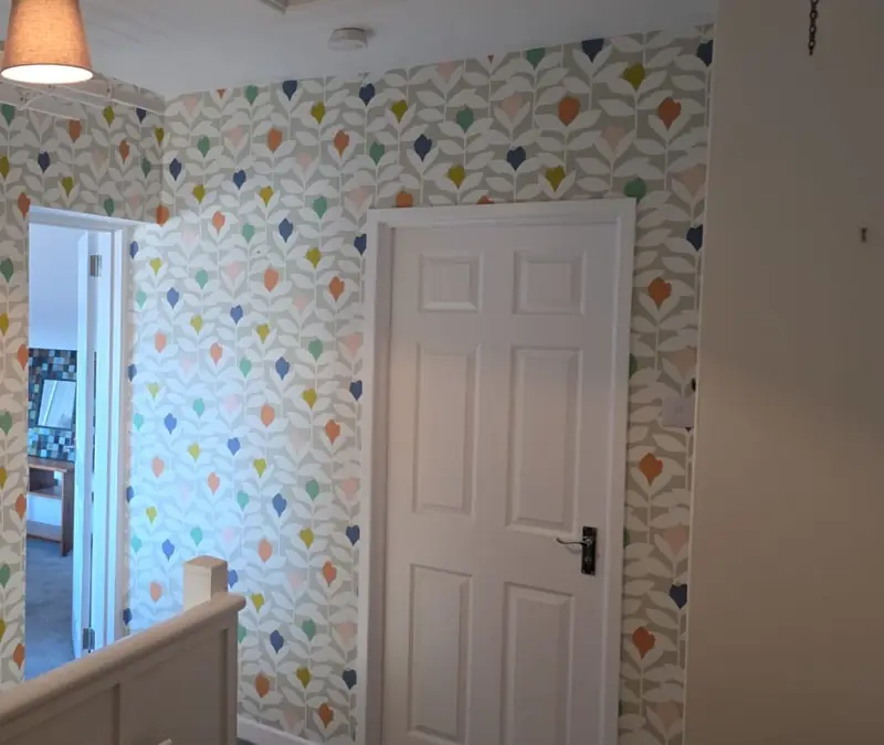 Landing papered in a bright geometric leaf pattern, with a white door and banister