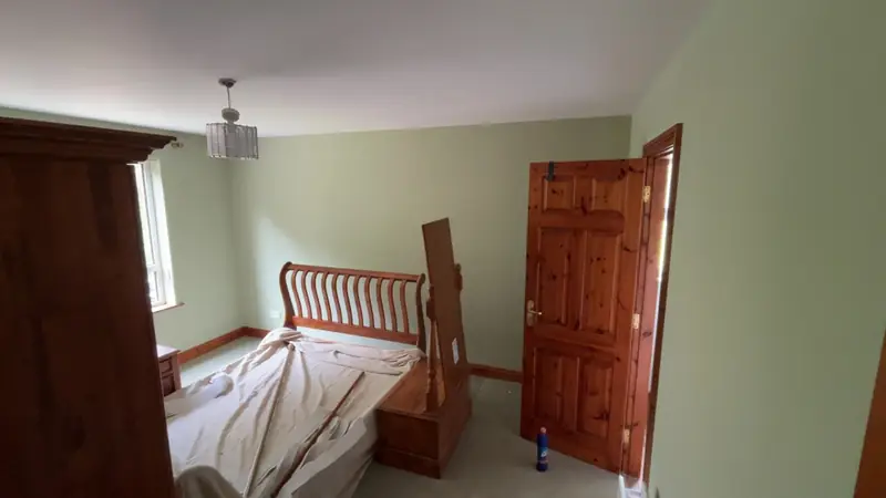 Bedroom freshly painted pale green, the furniture still covered with dust sheets
