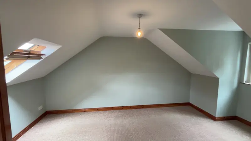 Attic bedroom finished in soft sage green with white ceilings and a roof window
