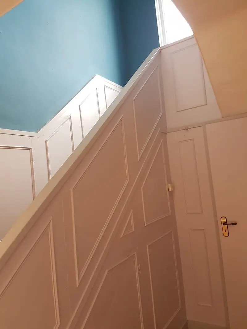 Staircase with painted wall panelling below and a deep teal wall above