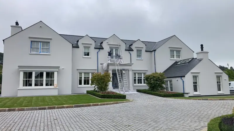 Front of a large white house with a ladder at one gable, a cobbled drive and neat hedges